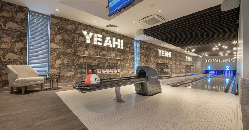 Modern bowling alley interior at Yeahi Bowling with red bowling ball on lane, blue pins, armchairs, and animal print walls.