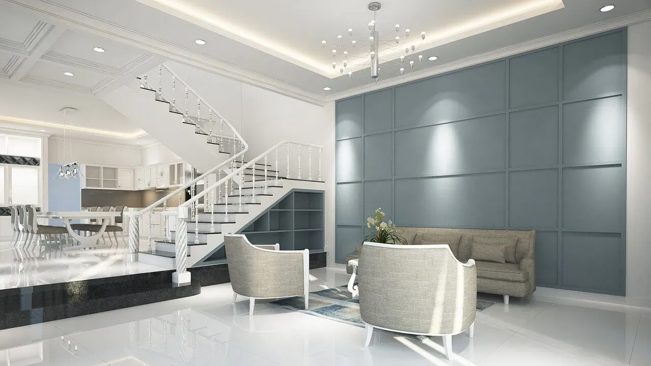 Modern luxurious living room with white curved armchairs, coffee table, blue accent wall, kitchen, and spiral staircase.