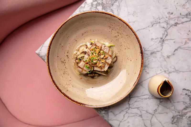 Close-up of mushroom and vegetable dish in terracotta bowl with small pitcher on marble surface near pink chair