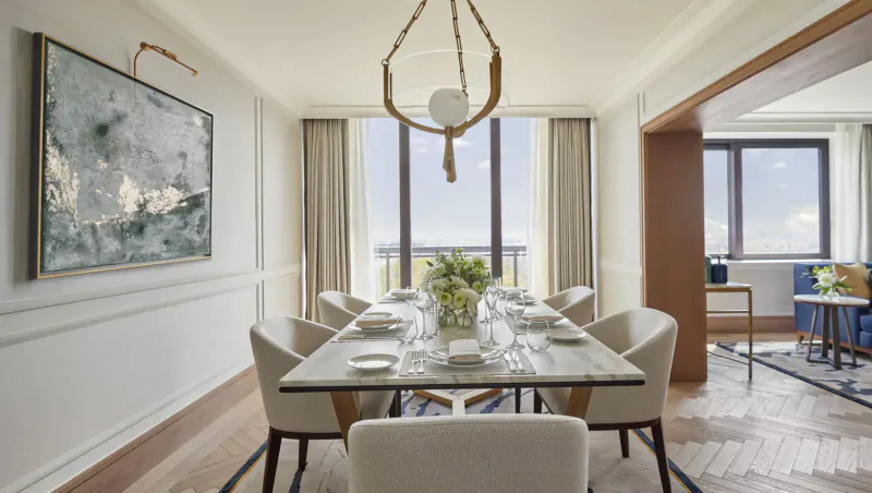 Elegant dining room in Carlton Tower Jumeirah Hotel with long marble table, chairs, pendant light, flowers, and city view windows.
