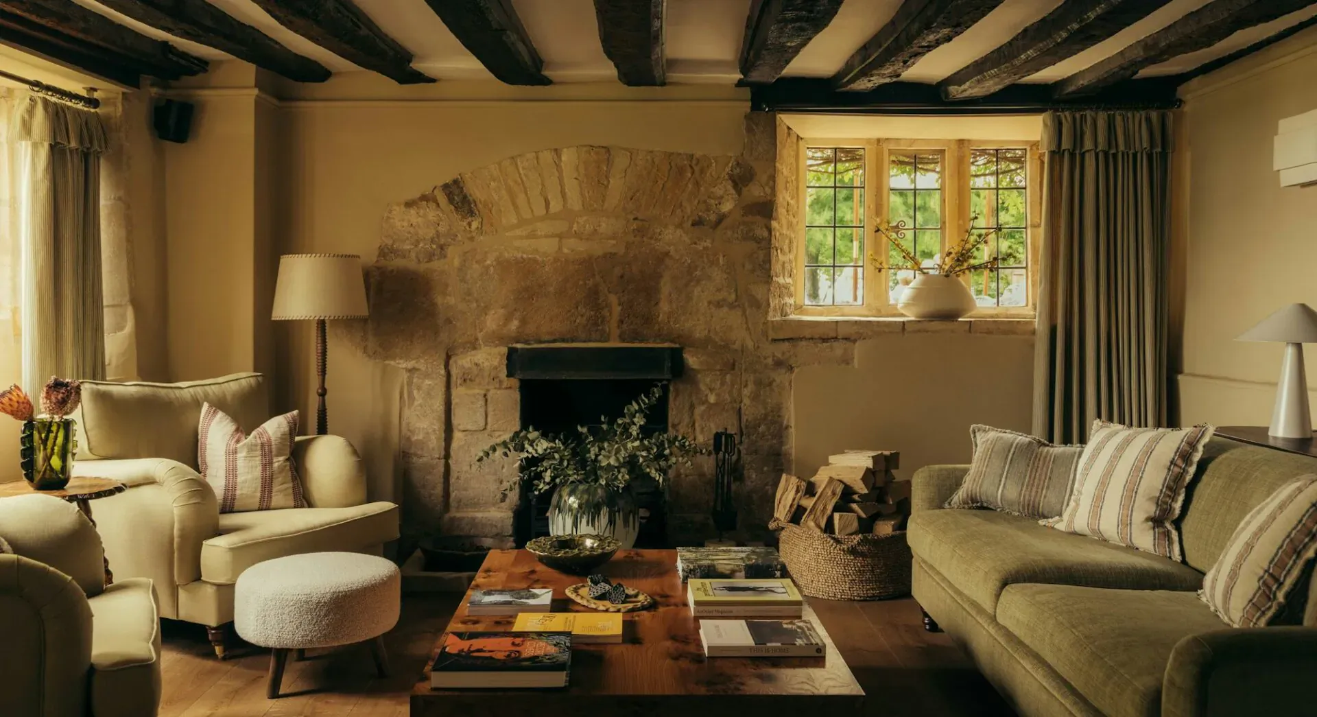 Cozy Cotswolds living room in Hyll with stone fireplace, green sofa, books, plants, and warm lighting