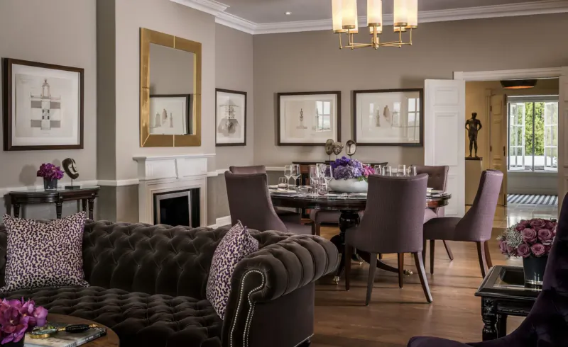 Elegant hotel dining room with tufted sofa, round table, purple flowers, chandelier, gilded mirror, and art in Johannesburg Westcliff.