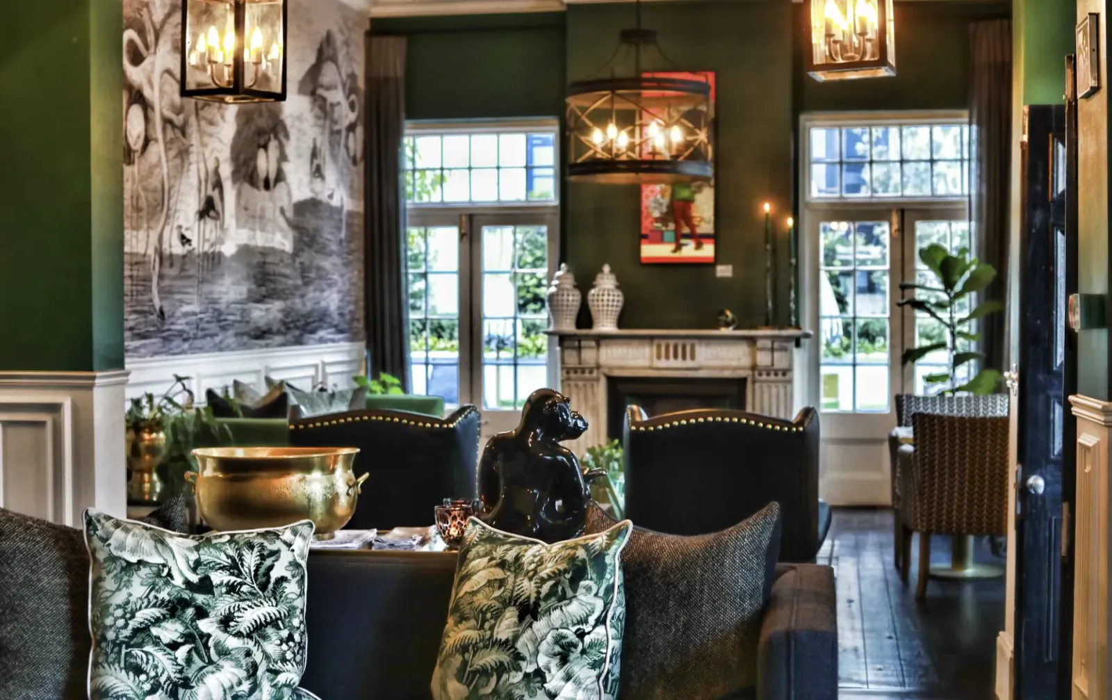 Elegant green lounge with fireplace, gorilla statue, patterned armchairs, brass bucket, and large windows