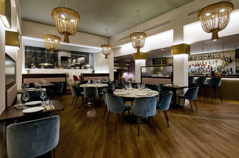 Elegant Kahani Indian restaurant interior with rattan pendant lights, velvet chairs, round tables set for dining, and stylish bar.