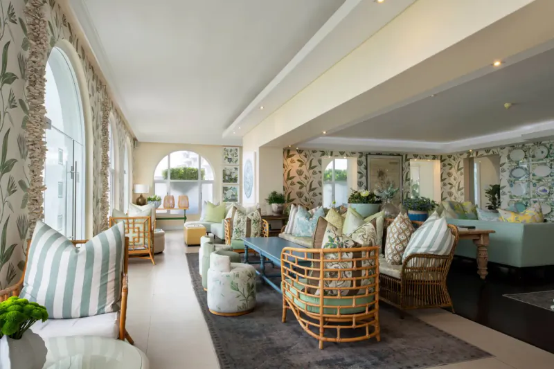 Elegant hotel lounge at The Marine with floral-upholstered wicker chairs, sofas, cushions, and plants in sunlit arched windows room.