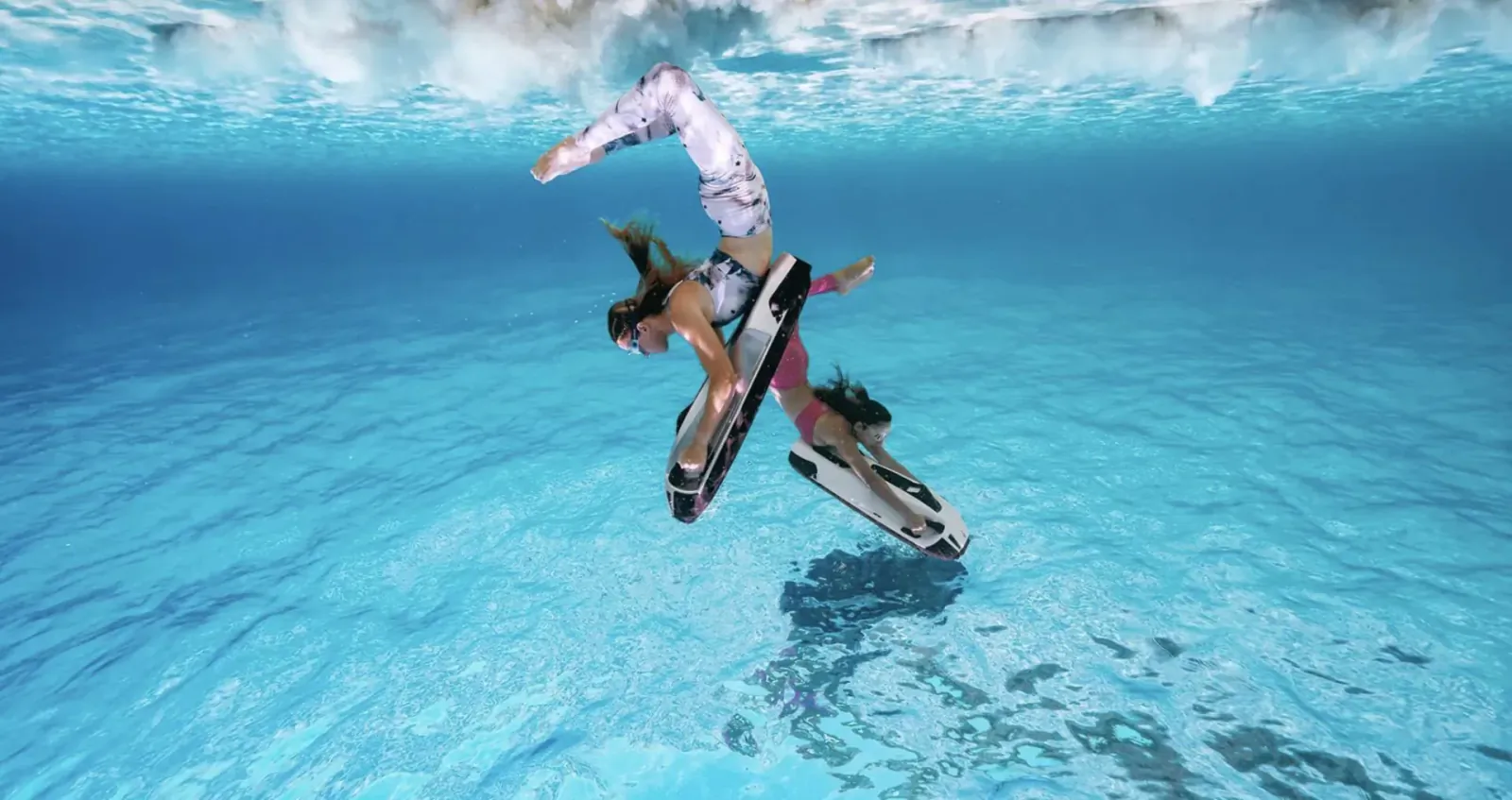 Woman in pink swimsuit riding powerful sea scooter underwater, performing dynamic flip in clear blue water