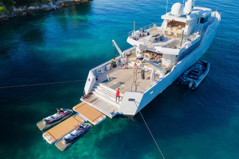 Aerial view of white luxury yacht 'Happy Me' anchored in turquoise waters near cliffs with jet skis on swim platform