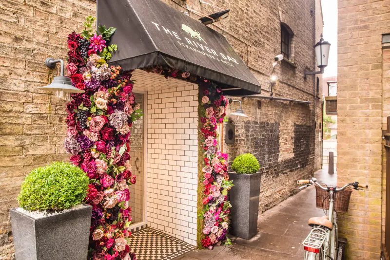 The Royal Spa entrance on brick alley, adorned with lush pink floral arches, awning, lanterns, and potted plants.