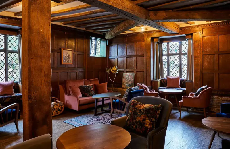 Cozy lounge in Hotel Indigo Stratford upon Avon with wood-paneled walls, beamed ceiling, plush armchairs, and small tables.