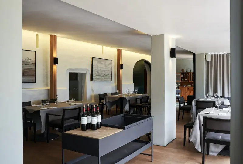 Elegant dining room at Clara’s Barn, Vergenoegd Löw, with wooden tables, red wine bottles, and arched doorway.