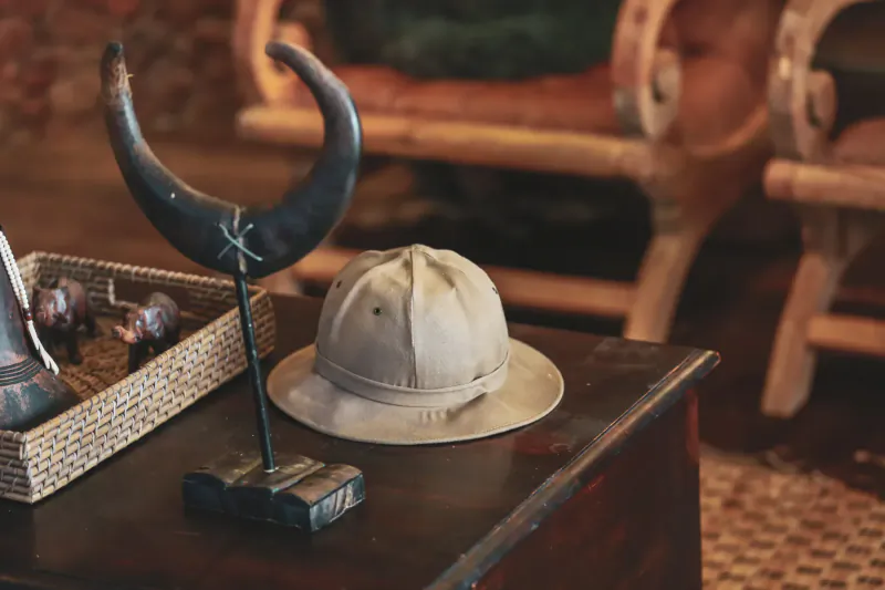 Pith helmet and curved horn on stand atop wooden table in Namibian gallery with bench backdrop