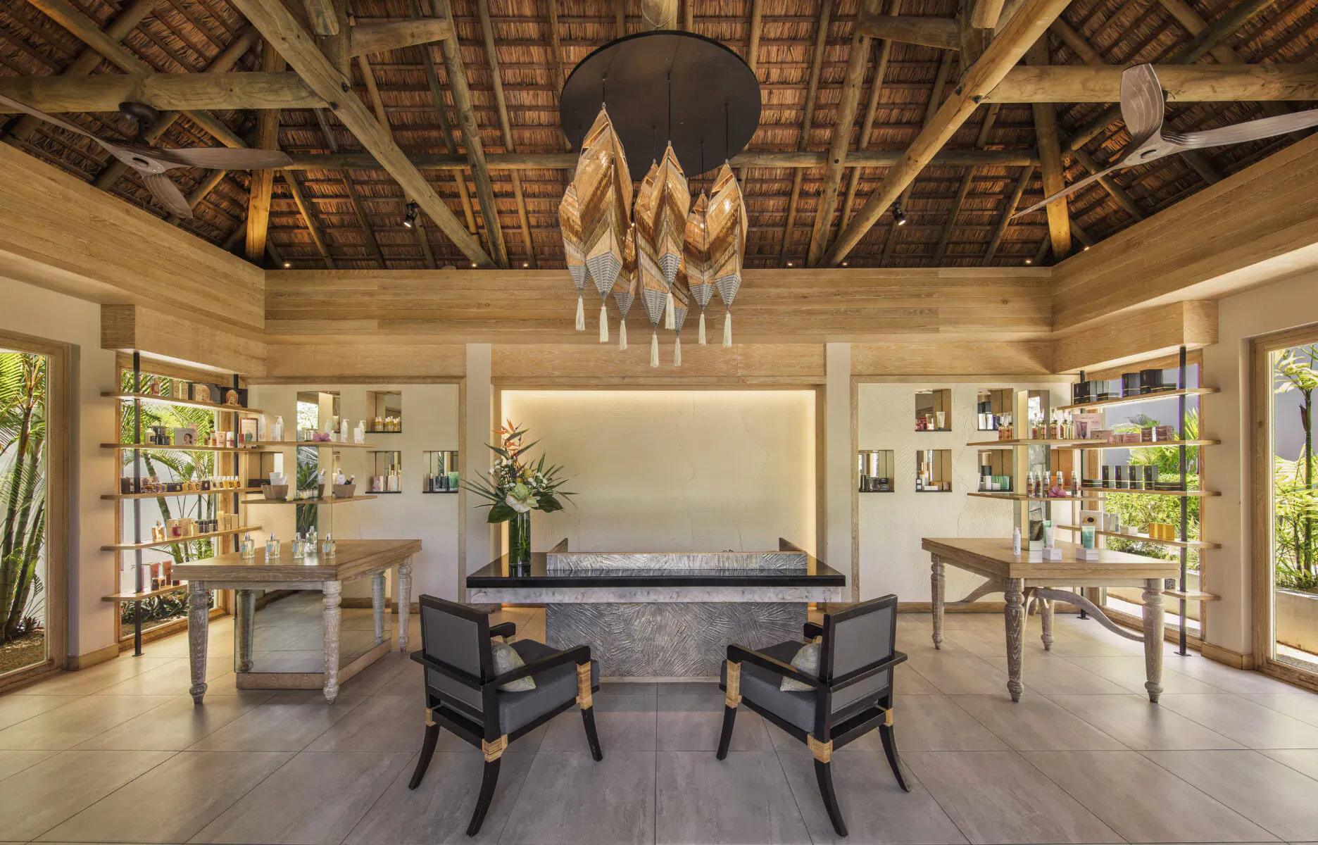 Elegant resort lobby with thatched ceiling, gold leaf chandelier, wooden shelves, plants, and rattan chairs at Anantara Iko Mauritius.