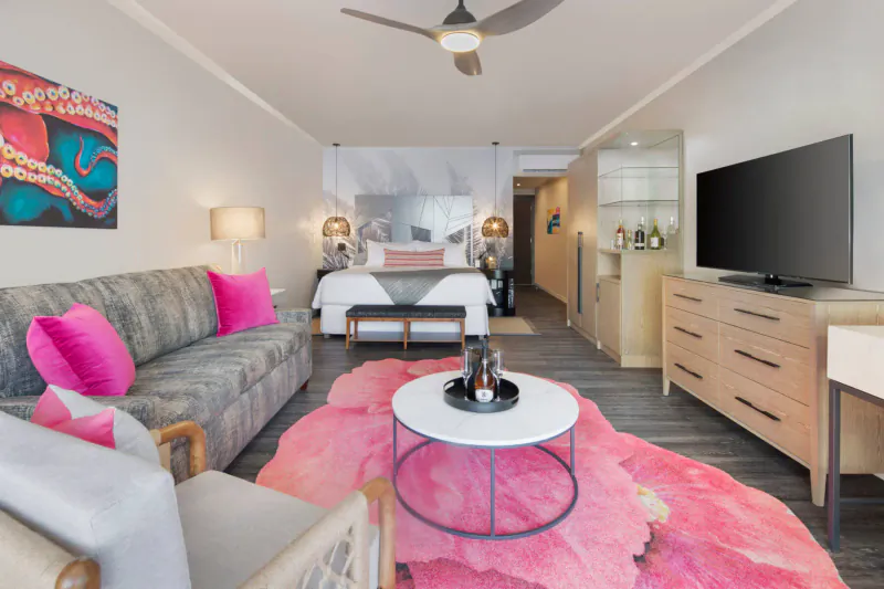 Spacious luxury beach suite with pink octopus art, gray sofa, pink rug, king bed, TV, and ceiling fan.