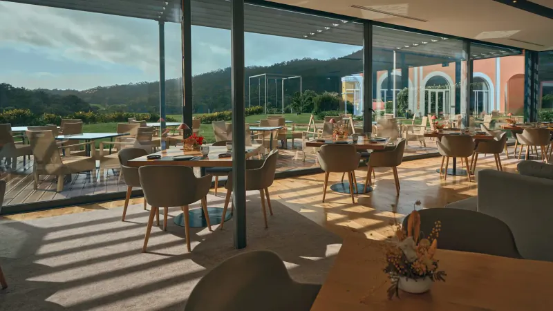 Spacious indoor-outdoor dining area at Penha Longa Resort with terrace seating, flower arrangements, and mountain views through glass walls.