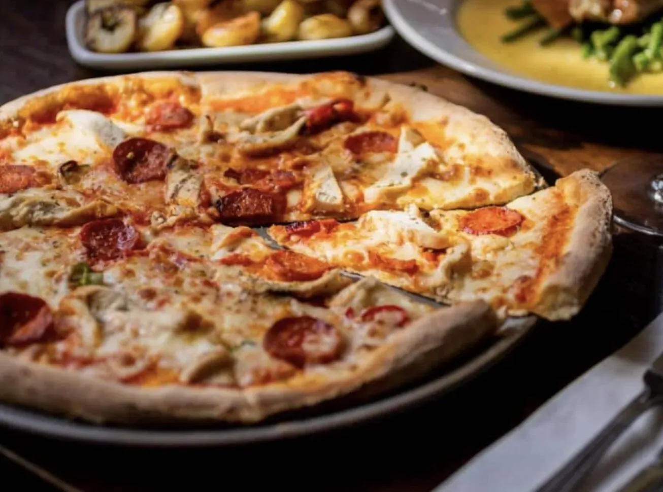 Pepperoni pizza with mushrooms and cheese on wooden table, beside side plates of potatoes and green beans