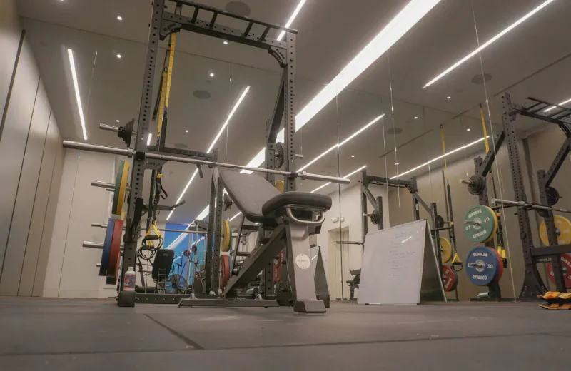 Modern gym with Eleiko squat racks, barbells loaded with colorful plates, and open collars securing weights.