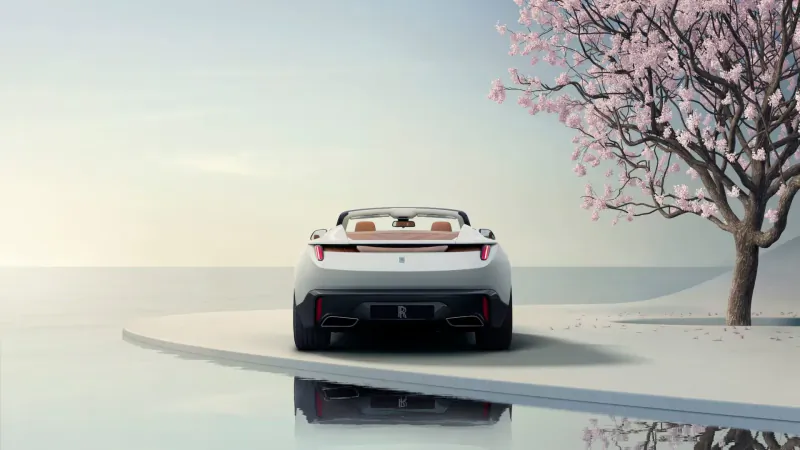 Rear view of white Rolls-Royce Arcadia Droptail convertible on curved road by water, cherry blossoms, serene reflection.