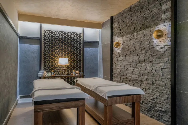 Luxurious Turkish spa room with two massage tables, stone walls, latticed screens, and warm lighting.