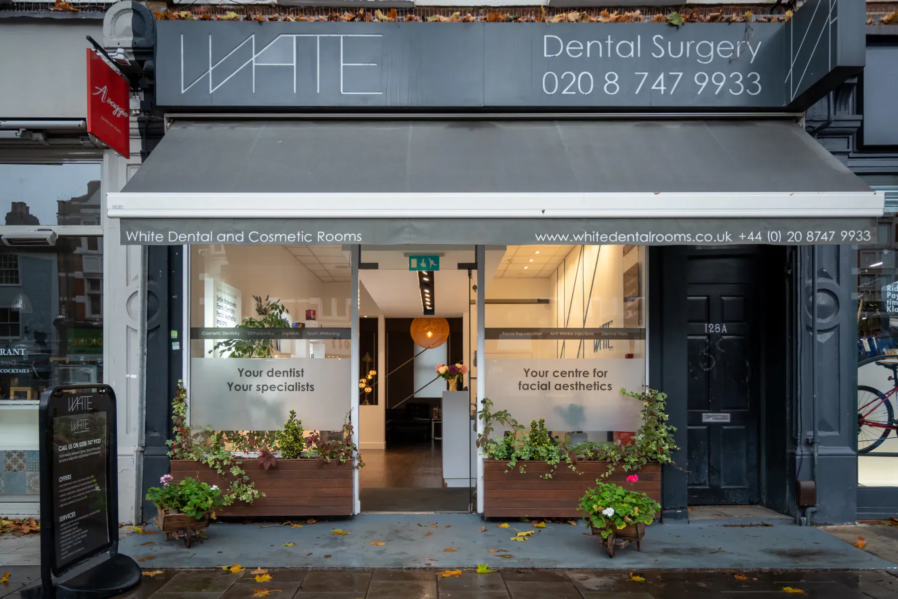 White Dental and Cosmetic Rooms exterior: modern storefront with signage, frosted windows, plants, phone 020 8747 9933, autumn street.