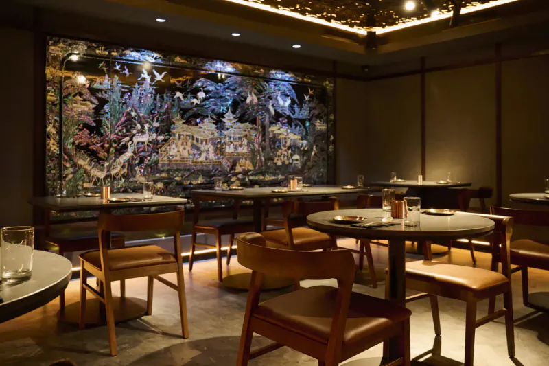 Elegant Korean restaurant interior with large colorful mural, wooden tables, chairs, and ambient lighting.