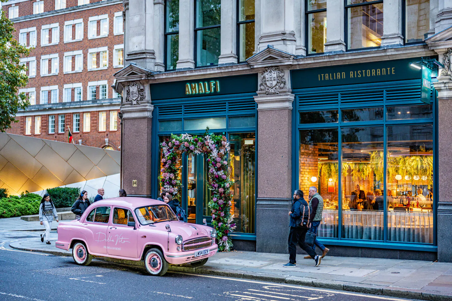 Pink vintage car parked outside Amalfi Italian Ristorante with floral decorations, urban street setting.