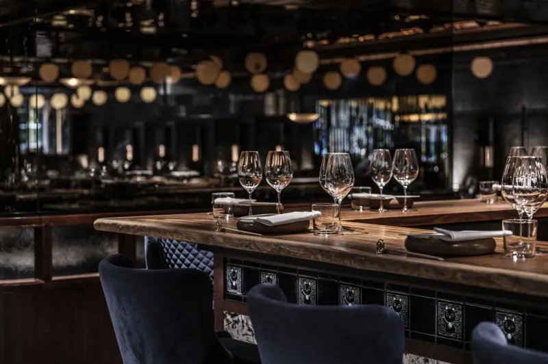 Elegant Lucky Cat Mayfair bar counter with wine glasses, napkins, ambient lighting, and mirrored walls.