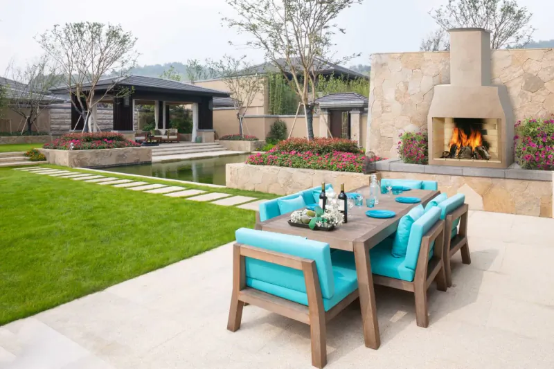 Outdoor turquoise patio dining table with wine bottles near stone Schiedel Isokern Volcanic Garden Fireplace blazing in landscaped yard