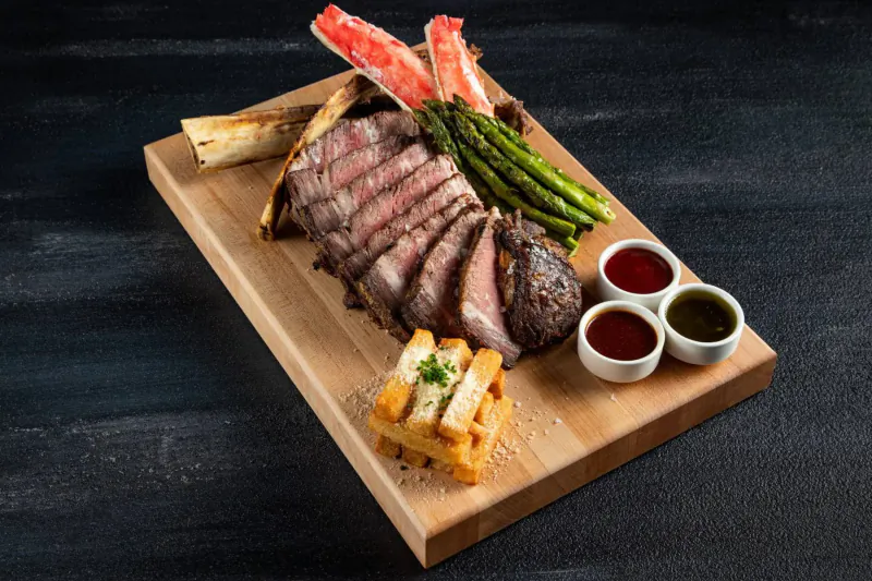 Sliced seared steak on wooden board with asparagus, king crab legs, fries, and sauce dips at STK.