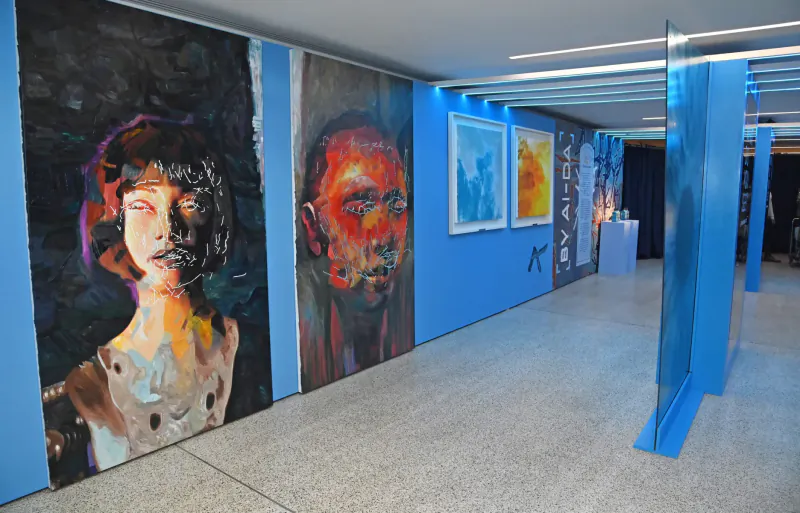 Gallery with large AI art portraits of a woman and man on blue walls, abstract paintings, at Design Museum event.