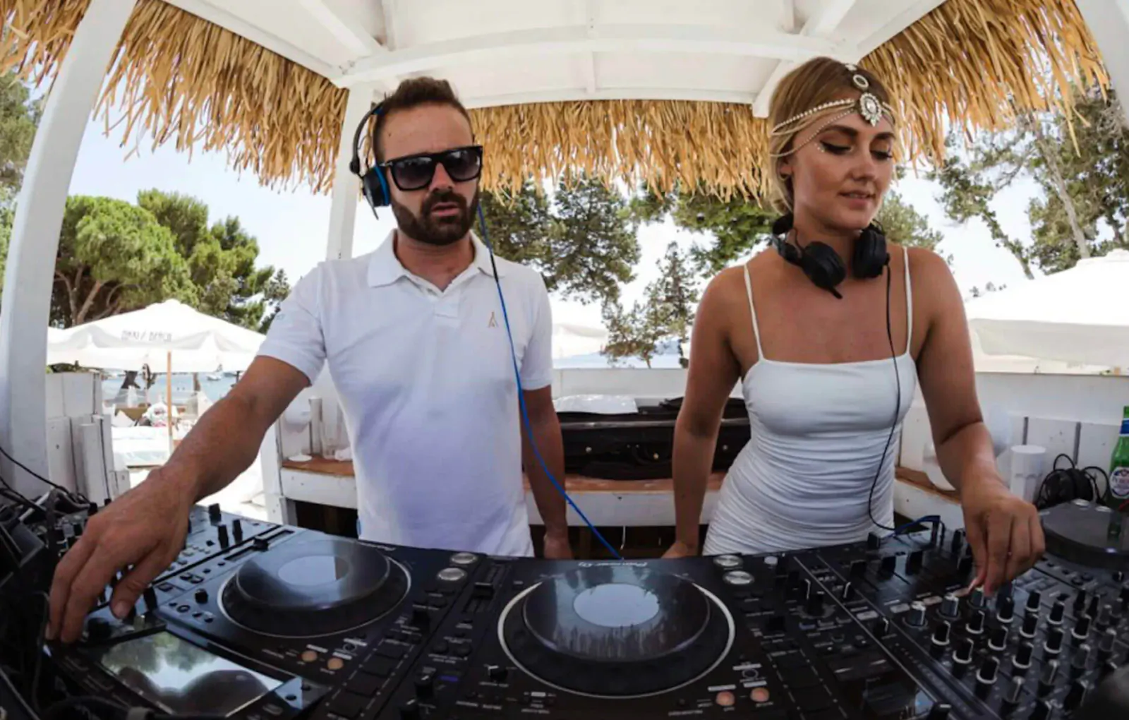 Man and woman DJs with headphones mixing tracks at Nikki Beach Ibiza beachfront tiki bar