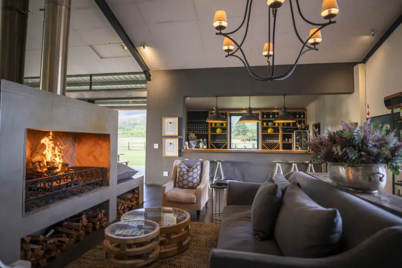 Cozy lounge at Kay and Monty Vineyard with blazing stone fireplace, gray sofa, bar, chandelier, and mountain view.