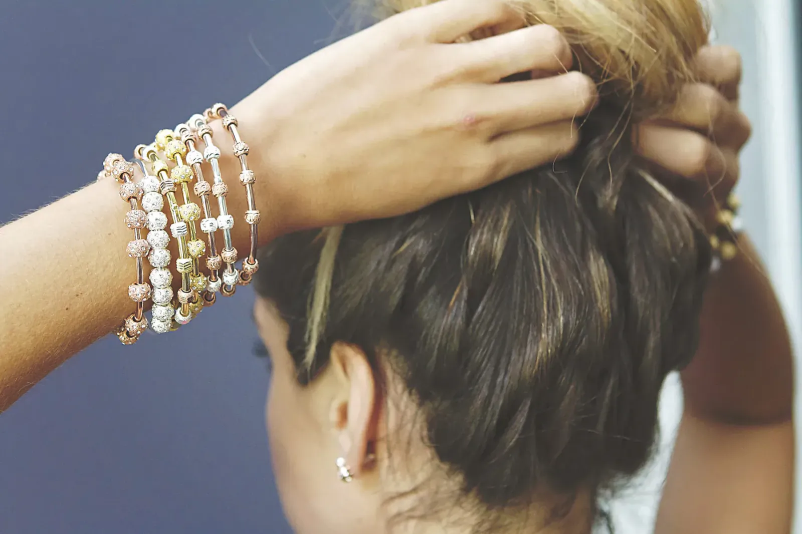Woman with bun hairstyle wearing stacked pearl and beaded bracelets by Chelsea Charles Jewelry, hand on hair