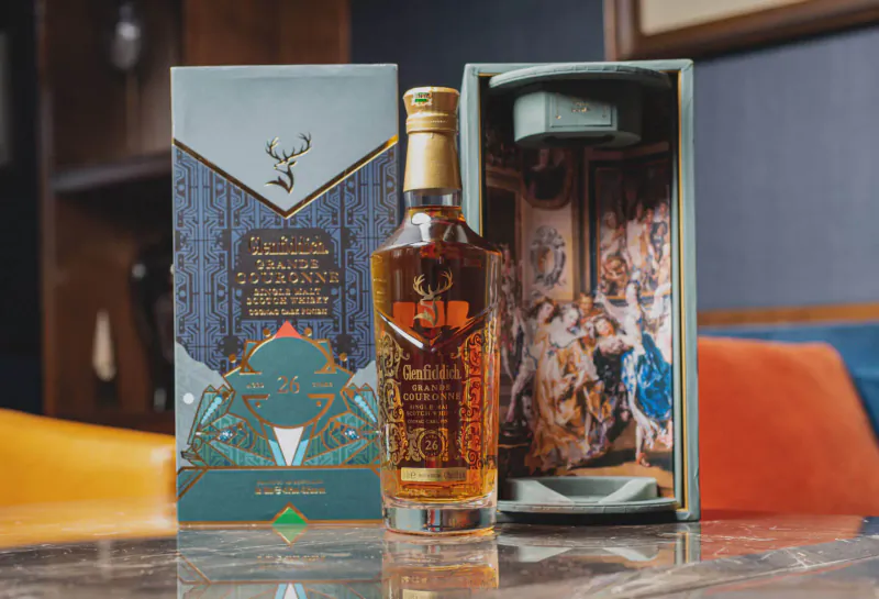 Glenfiddich whisky bottle in open box with Kenyan artist Wisetwo's gallery artwork collaboration, on table.