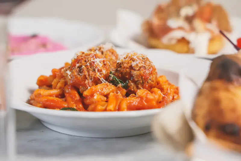 Close-up of Sicilian spaghetti with meatballs in tomato sauce, garnished with basil, on white plate at rooftop table