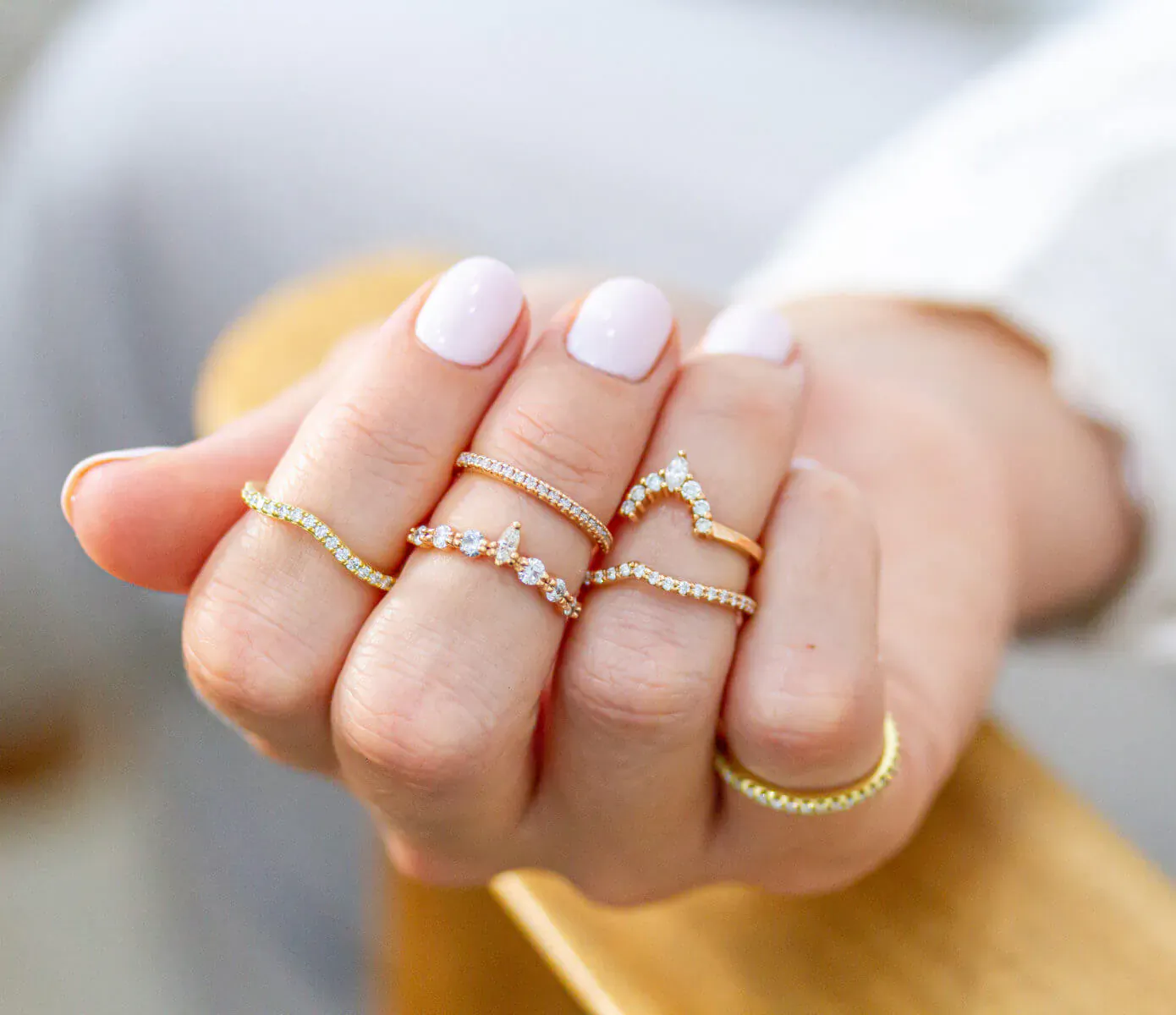 Woman's hand displaying multiple gold diamond rings, including stacked bands and V-shaped designs, on white background