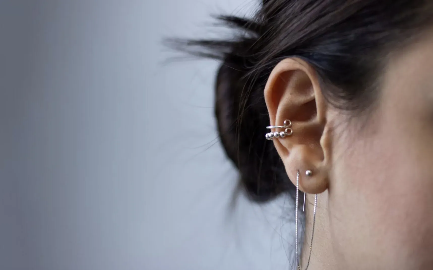 Close-up of woman's ear with silver hoop and dangling fringe earrings, hair in bun