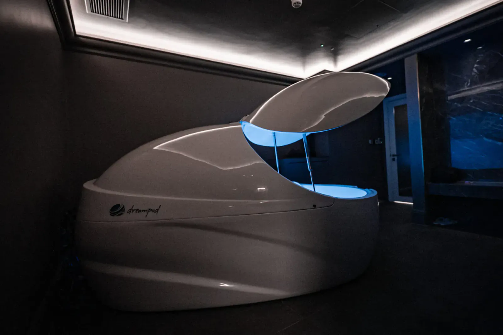 Open Dreampod float tank with blue glowing water in modern spa room at The Body Lab.