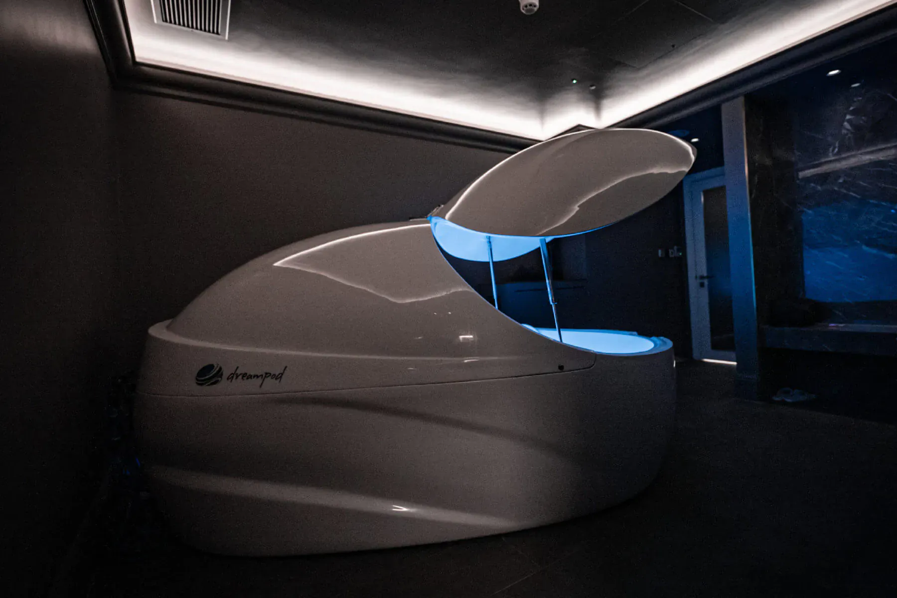 Open Dreampod float tank with blue glowing water in modern spa room at The Body Lab.