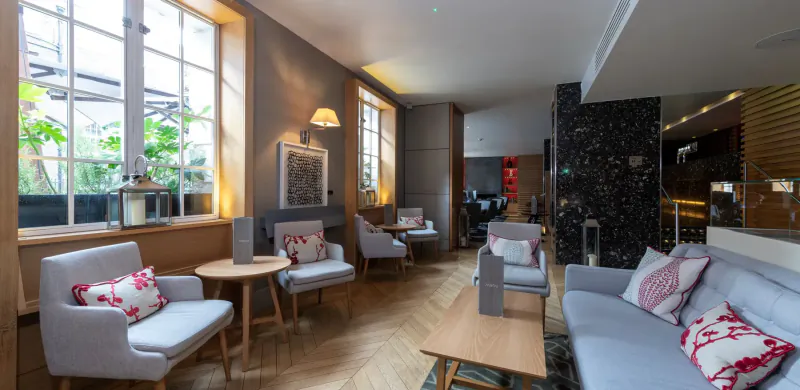 Cozy hotel lounge at Apex Temple Court with gray armchairs, floral cushions, wooden tables, large windows, and plants.