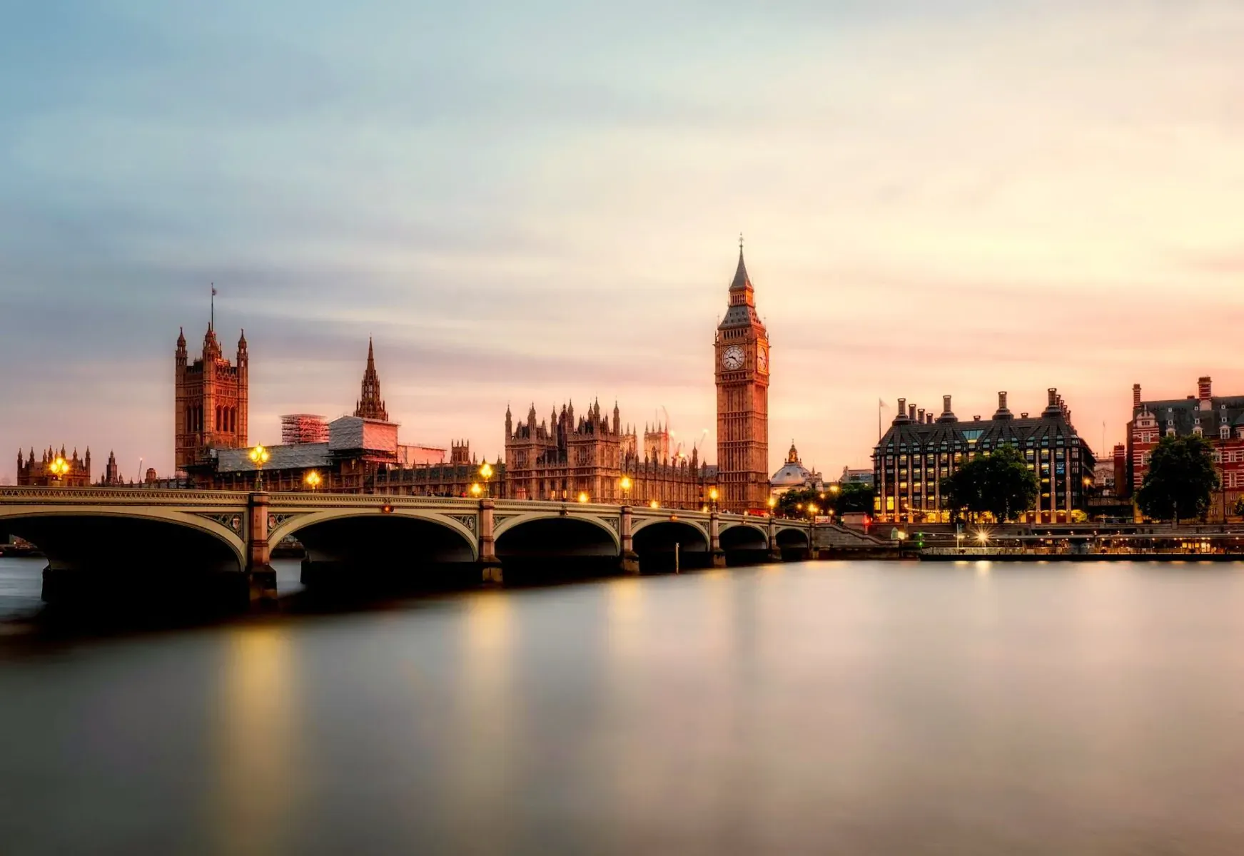 Big Ben and Houses of Parliament across Thames River bridge at sunset, bokeh effect