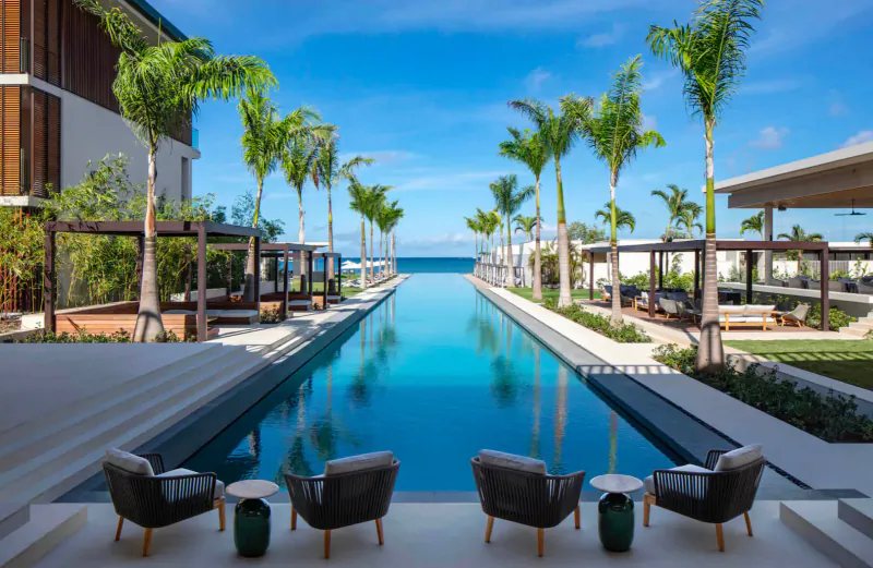 Infinity pool at Silversands Grenada flanked by modern white villas, palm trees, lounge chairs, and turquoise ocean horizon.