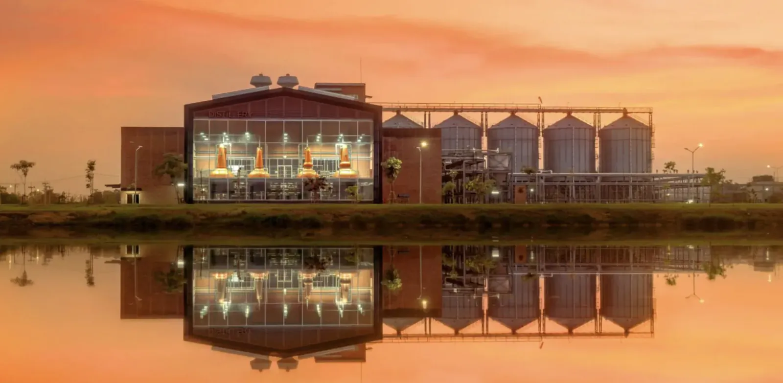 Prakaan Whisky distillery with grain silos reflected in water at sunset