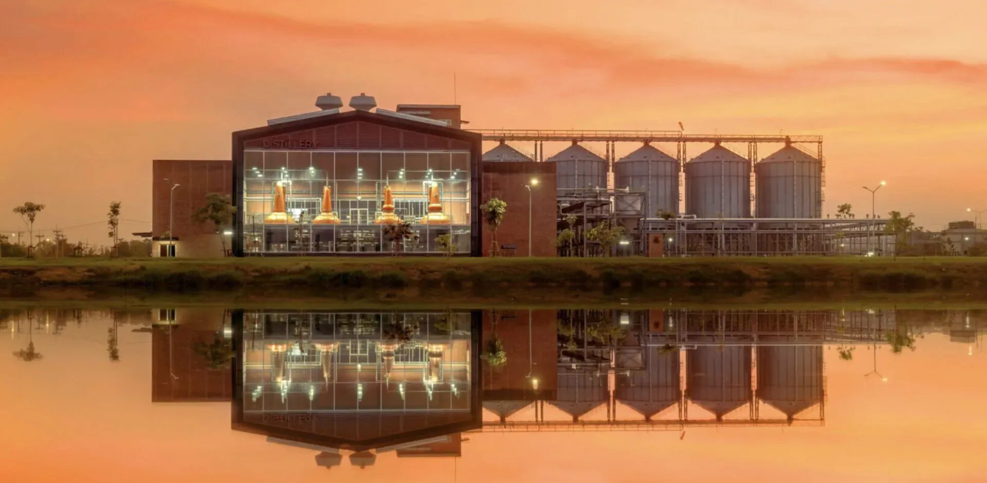 Prakaan Whisky distillery with grain silos reflected in water at sunset
