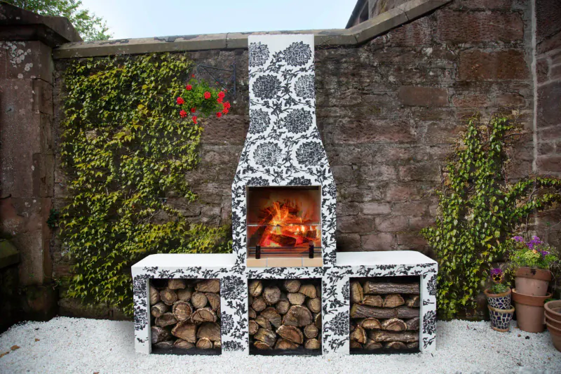 Schiedel Isokern Volcanic Garden Fireplace with floral-patterned design, burning fire, stacked logs, against ivy-covered stone wall.