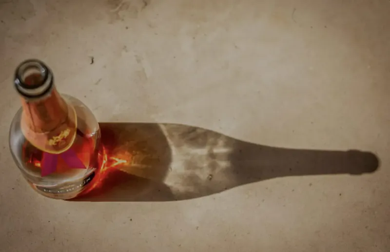Orange-tinted wine bottle with pink star label casting long shadow on beige surface