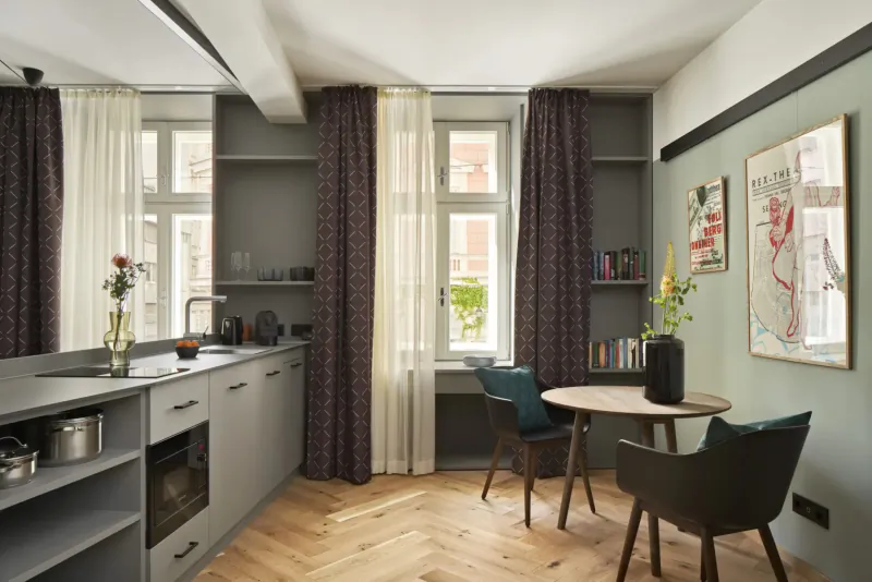 Modern Vienna apartment kitchen with gray cabinets, round table with green chairs, flowers, and abstract wall art.