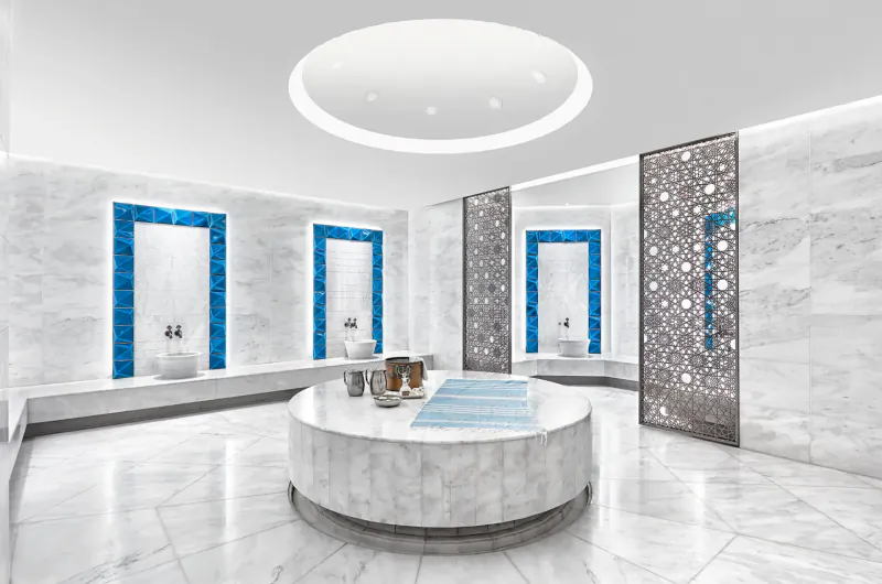 Elegant marble Turkish hammam at Naturelife Spa with blue-tiled basins, central round table, and ornate dividers