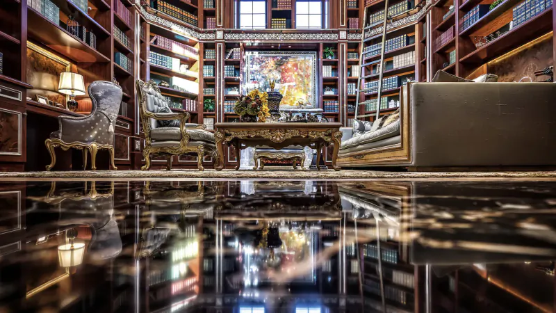 Luxurious library interior with ornate wooden bookshelves, armchairs, gilded desk, large abstract painting, and polished reflective floor.