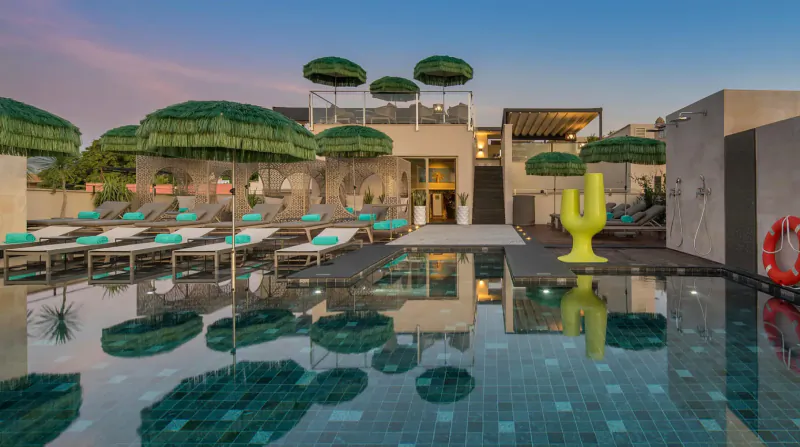 El Llorenç Parc de la Mar hotel poolside at sunset with green umbrellas, loungers, yellow cactus sculpture, and calm turquoise water.