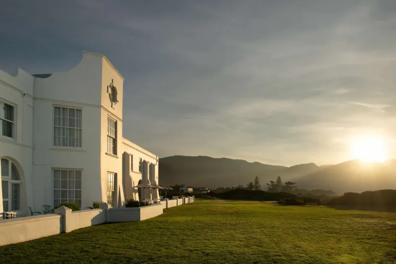White mansion of The Marine hotel at sunset with mountains and green lawn in South Africa